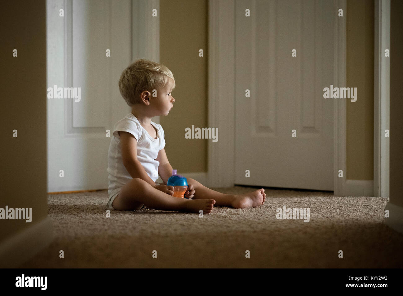 Cute boy avec une bouteille d'eau à l'écart tout en étant assis sur un tapis à la maison Banque D'Images