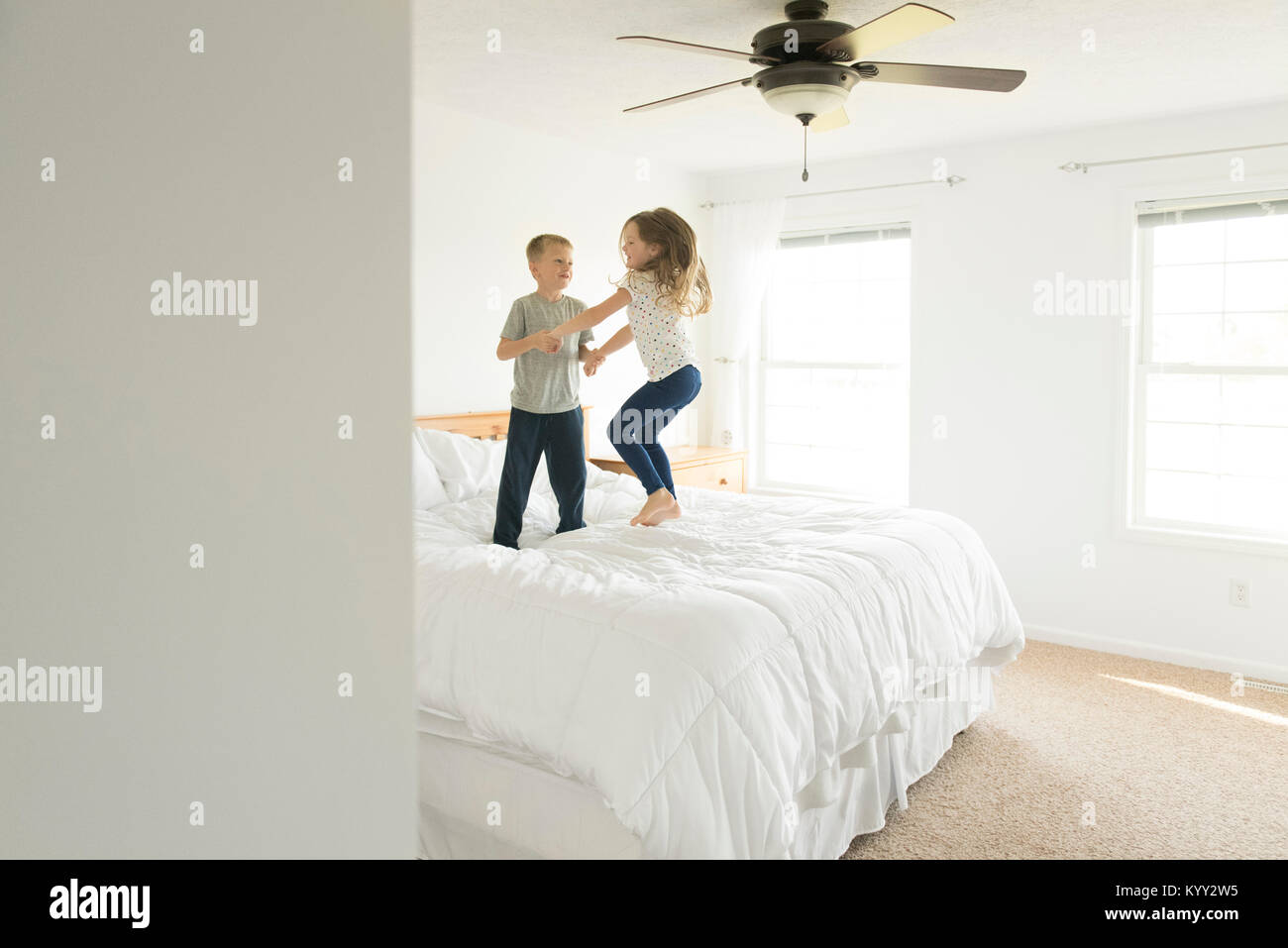 Frères et sœurs se tenant la main tout en sautant sur le lit Banque D'Images