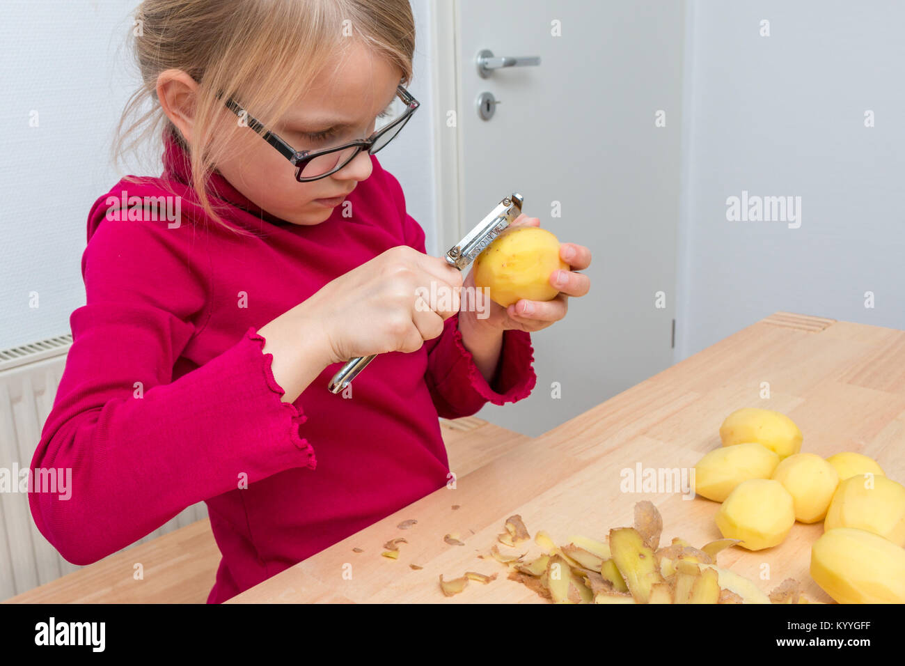 Une fille épluche une pomme de terre avec un couteau économe. Pull rouge a Banque D'Images