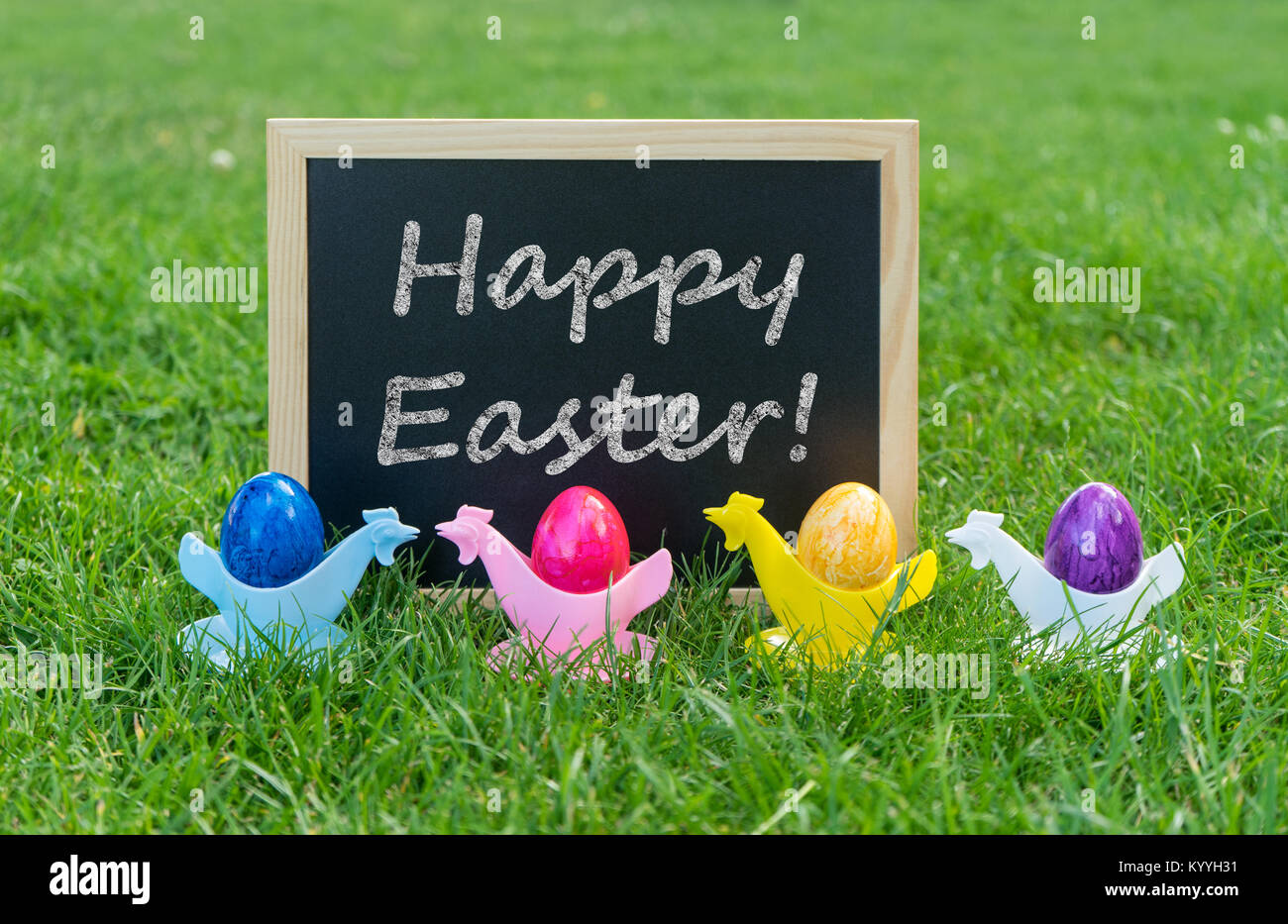 Eastercard avec tableau noir et les oeufs de Pâques colorés à egg cups sur un pré Banque D'Images