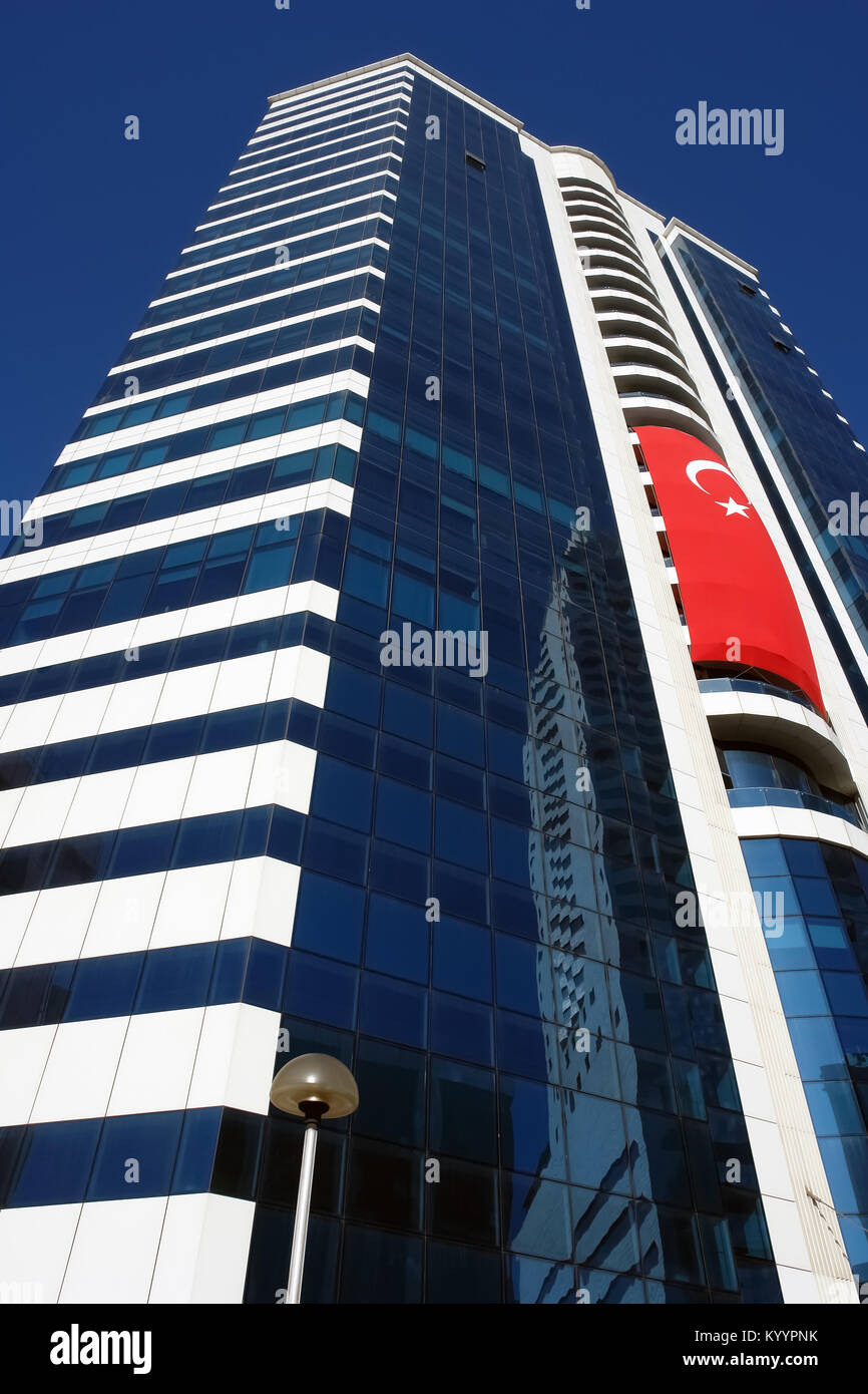 Bâtiment moderne de plusieurs étages de haut avec un grand drapeau turc contre le ciel bleu à Izmir, Turquie. Banque D'Images