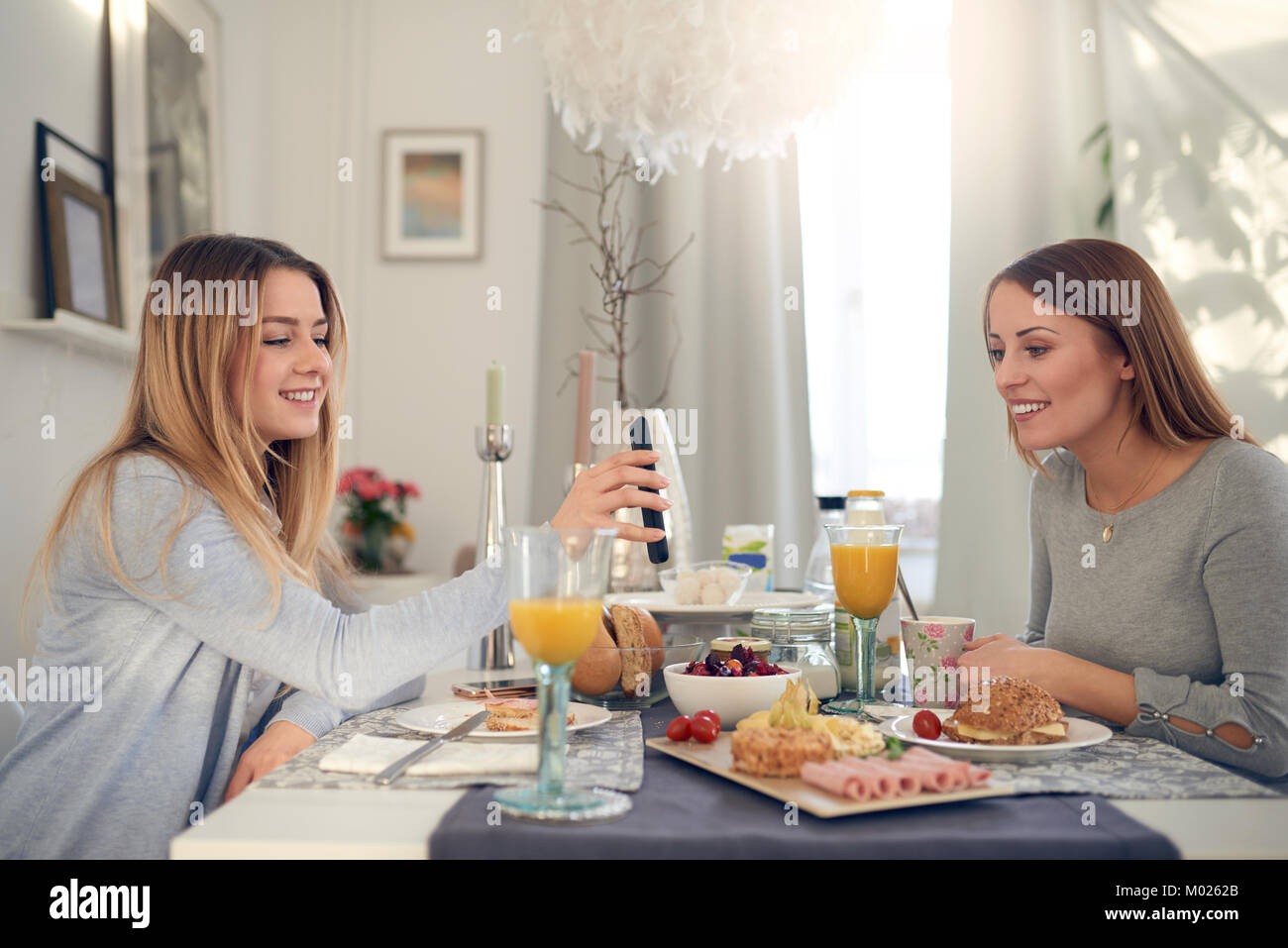 Smiling attractive jeune adolescent montrant sa mère son téléphone portable en bénéficiant d''un petit-déjeuner sain à l'intérieur ensemble à la maison Banque D'Images