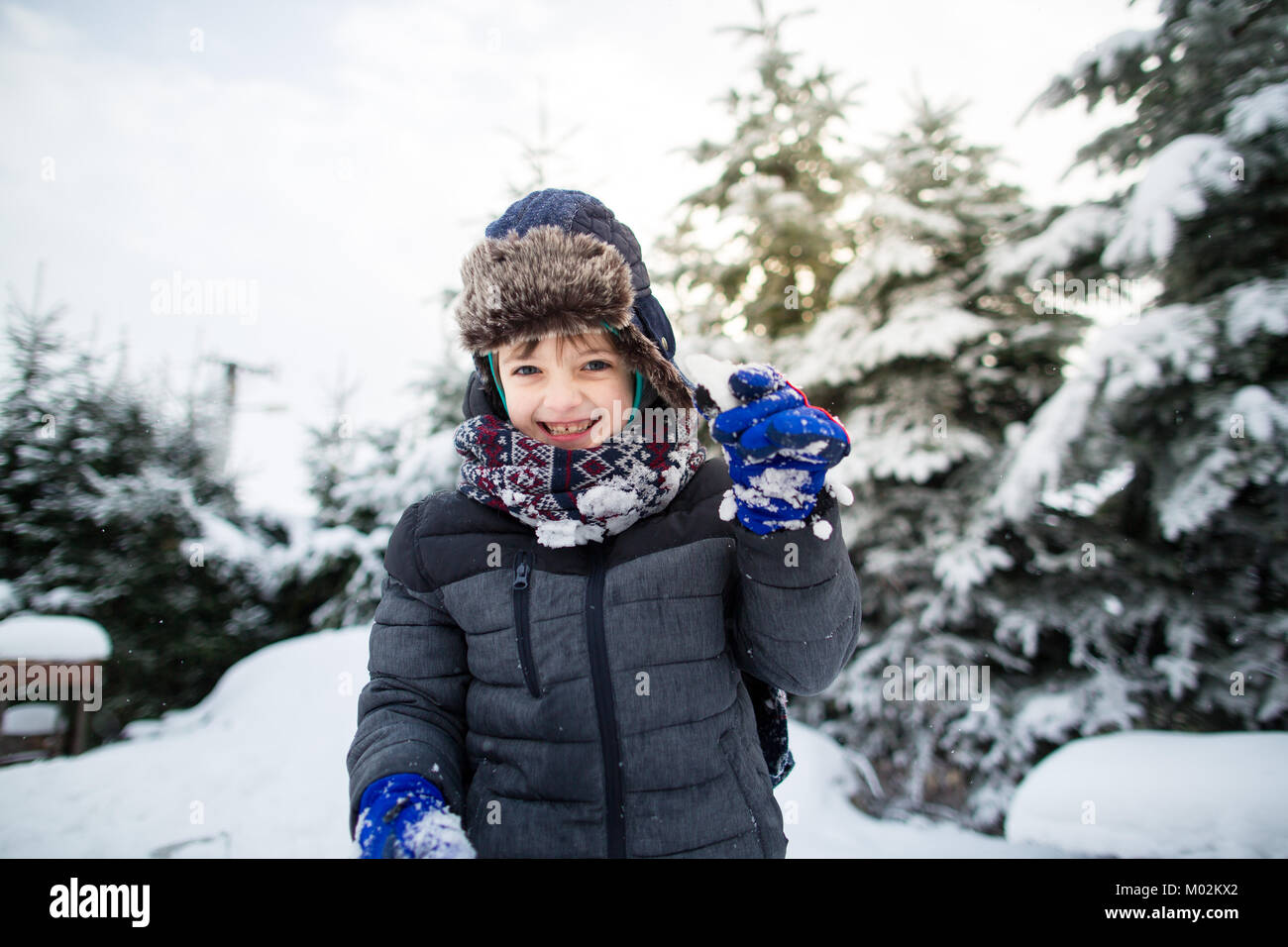 Vue de face d'un enfant souriant dans des vêtements chauds s'amusant dans un jardin enneigé. Garçon profitant de la neige en hiver. Banque D'Images