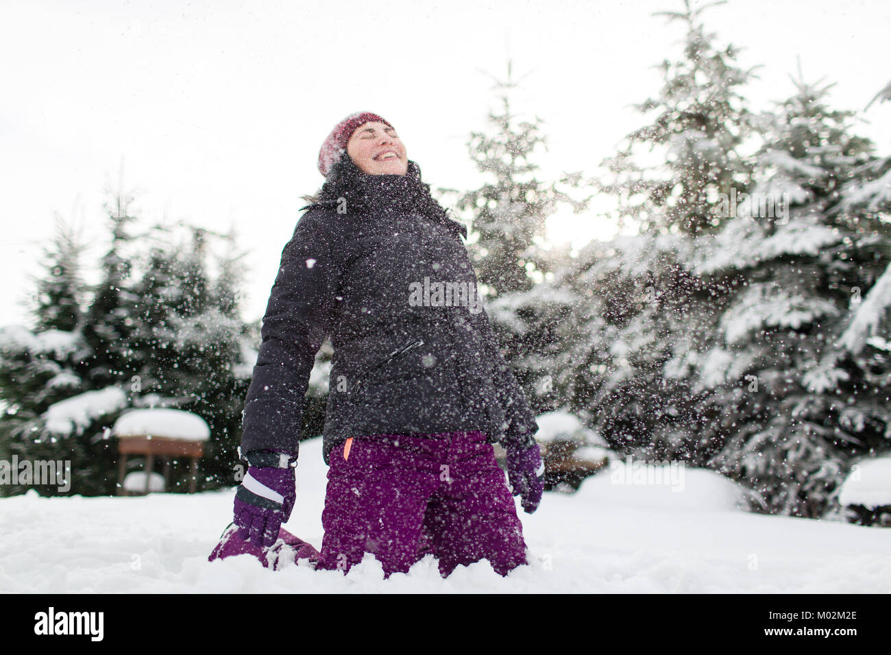 Laughing woman en vêtements chauds d'hiver assis sur sol enneigé avoir son visage frappé par la neige. Woman snow. Banque D'Images