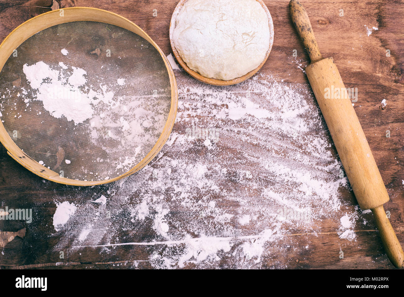 La pâte dans un bol en bois et une grille ronde vintage avec un rouleau à pâtisserie, vue du dessus Banque D'Images