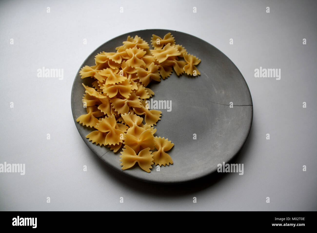 Pâtes Farfalle lune figure isolée sur un côté de la plaque de béton gris Banque D'Images