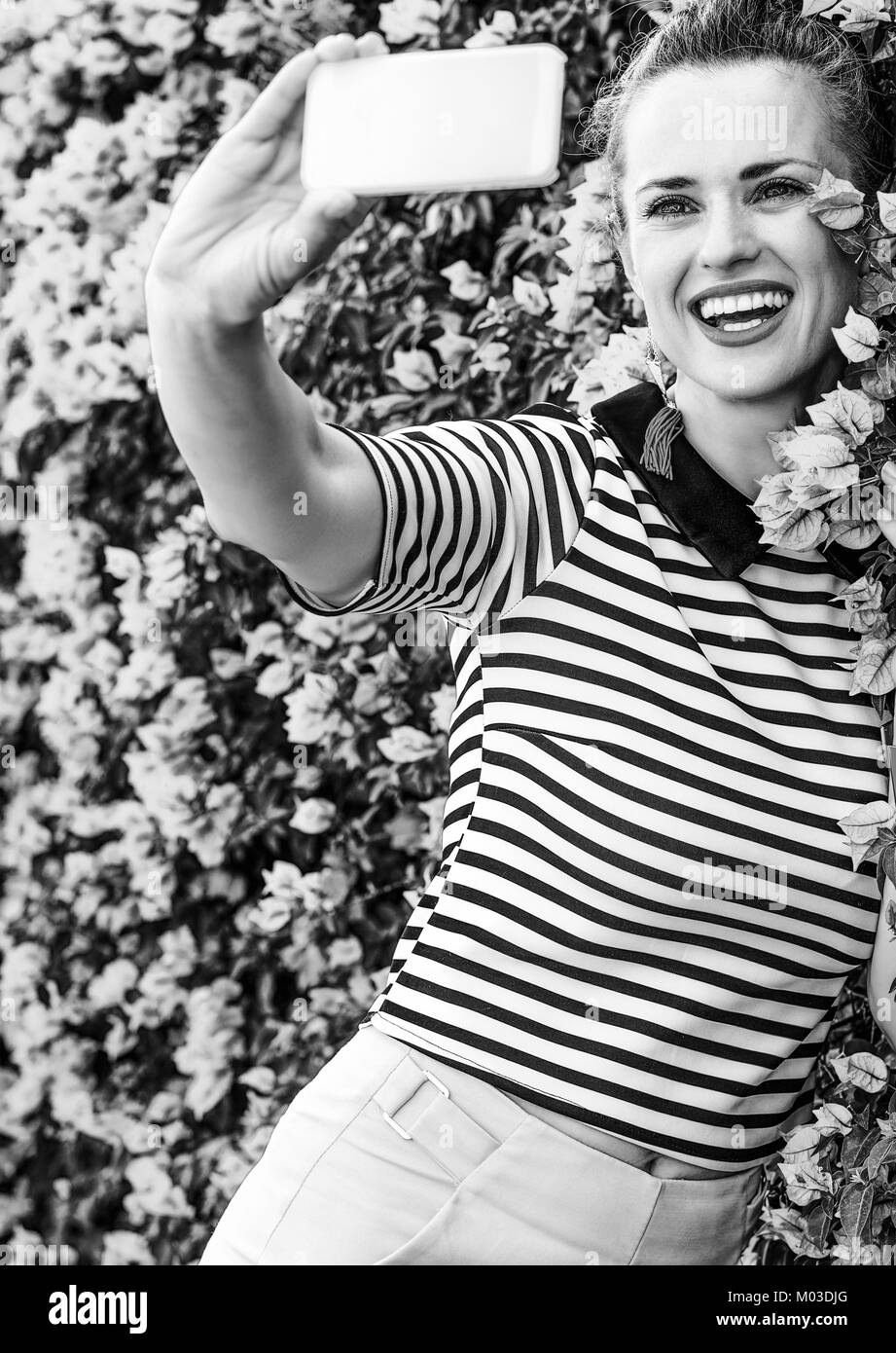 Fraîcheur colorée. smiling woman in élégant short jaune et stripy shirt coloré fleurs magenta près de lit avec prise téléphone selfies Banque D'Images