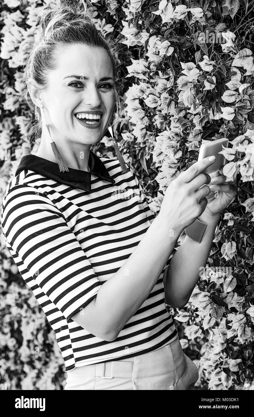 Fraîcheur colorée. bonne femme la mode en short jaune et stripy shirt against colorful fleurs magenta bed avec le smartphone taking photo Banque D'Images