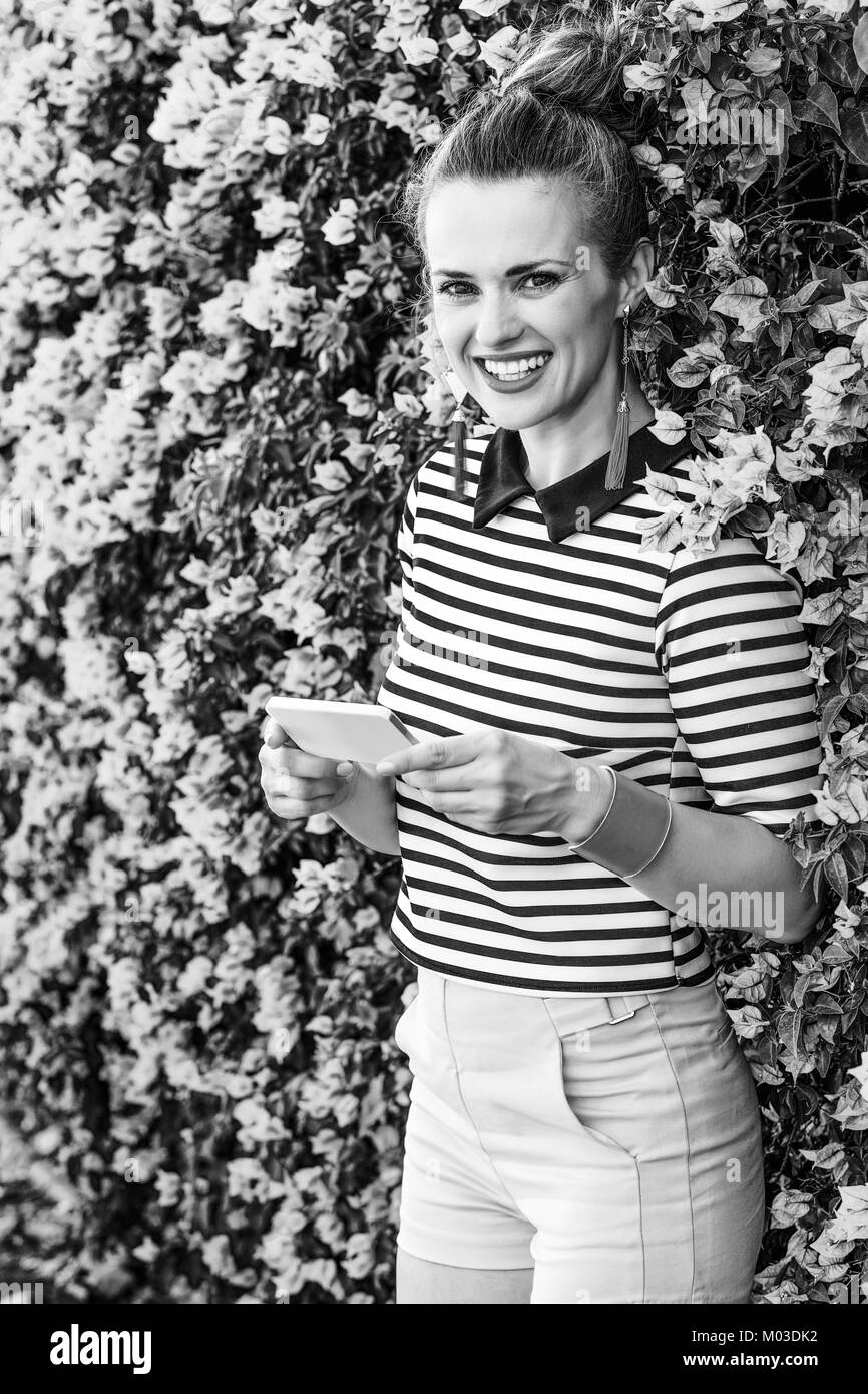 Fraîcheur colorée. smiling femme moderne en short jaune et stripy shirt against colorful fleurs magenta bed écrit sms Banque D'Images