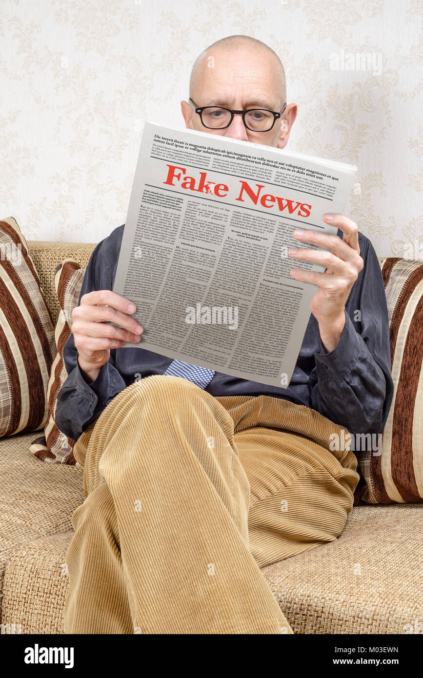 Un homme portant des lunettes est assis sur un canapé à la maison, lire un journal de rapports faux news. Faux texte Lorem ipsum. Banque D'Images
