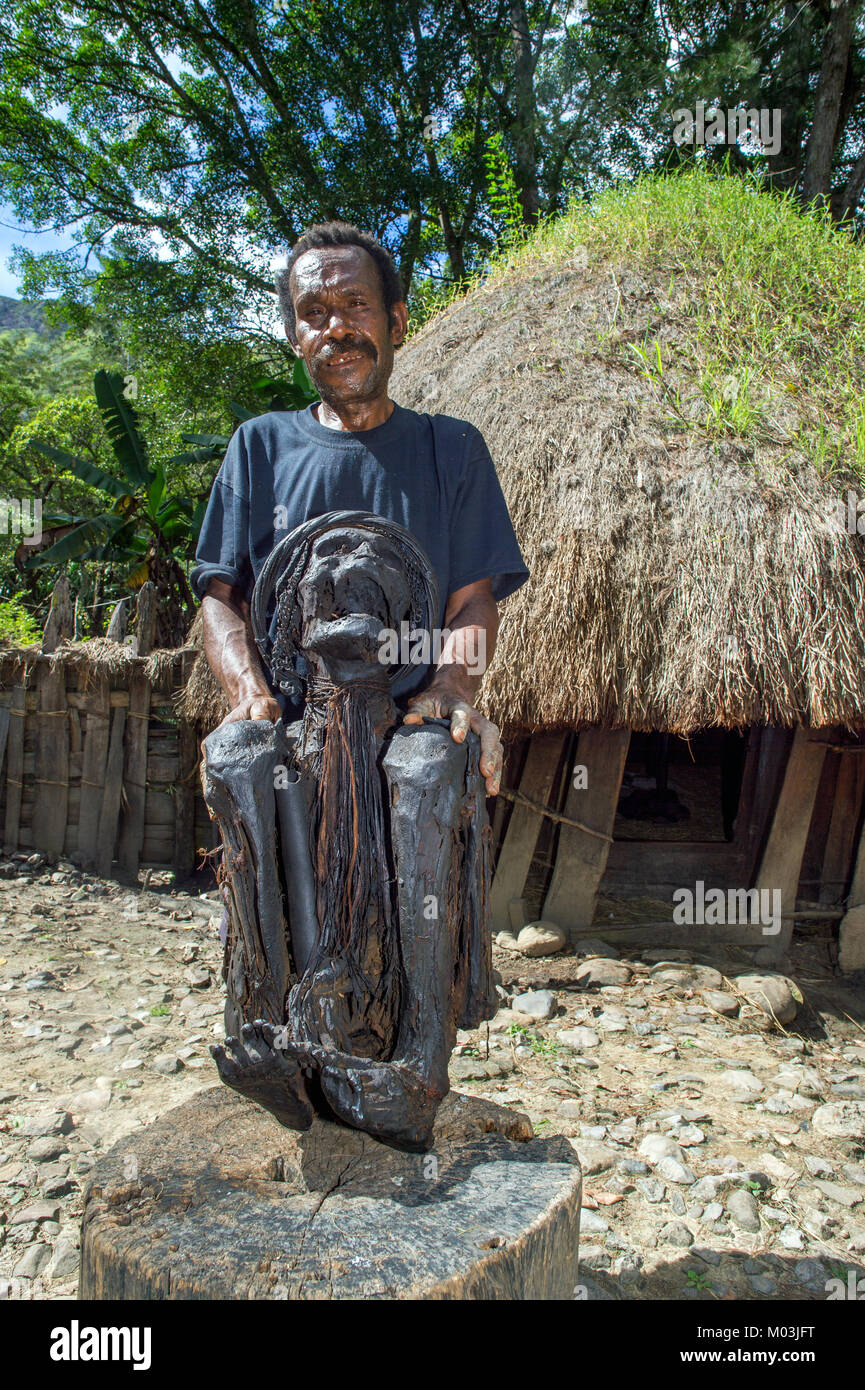 Vieil homme en face d'une maison traditionnelle montrant une momie d'un ancien du village maman présenté par un membre de la tribu de Dali, près de la ville de Wamena à Bali Banque D'Images