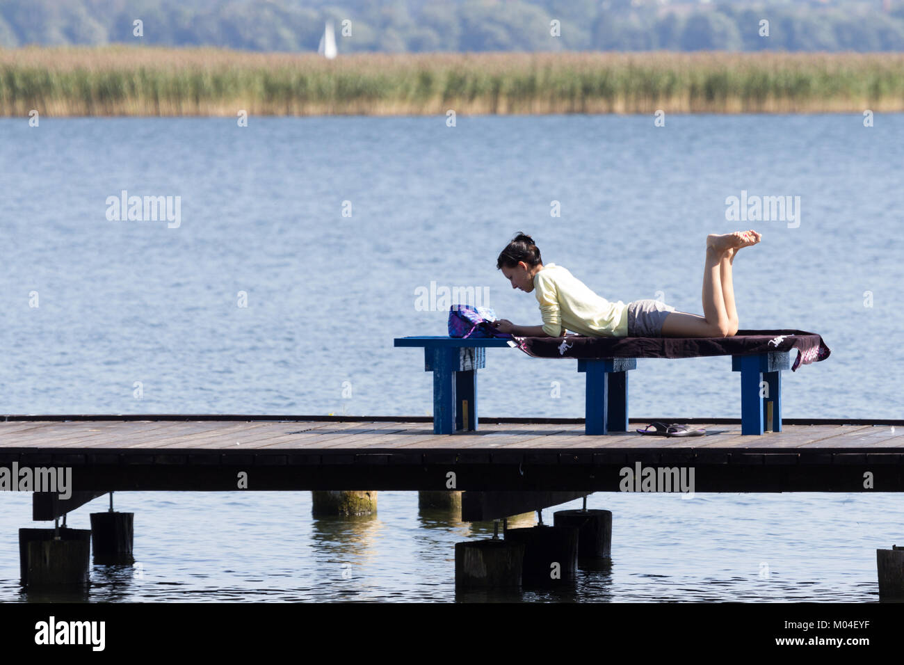 La femme est couchée sur un banc près du lac et la lecture d'un livre. Wilkasy, la Mazurie, Région des lacs Big, Pologne Banque D'Images