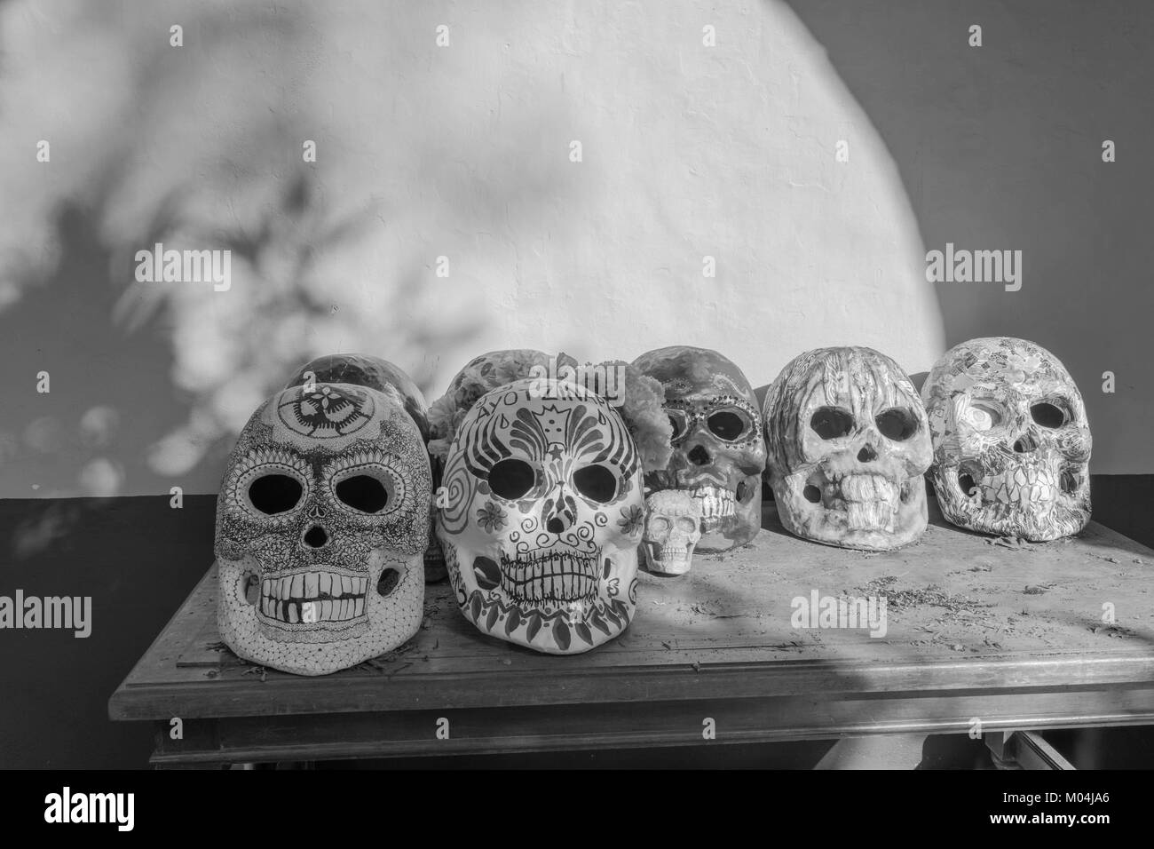 Sept grandes et une peu de crânes peints sur une table avec des ombres projetées sur le mur, en noir et blanc, pour le Jour des Morts au Mexique, célébration Banque D'Images