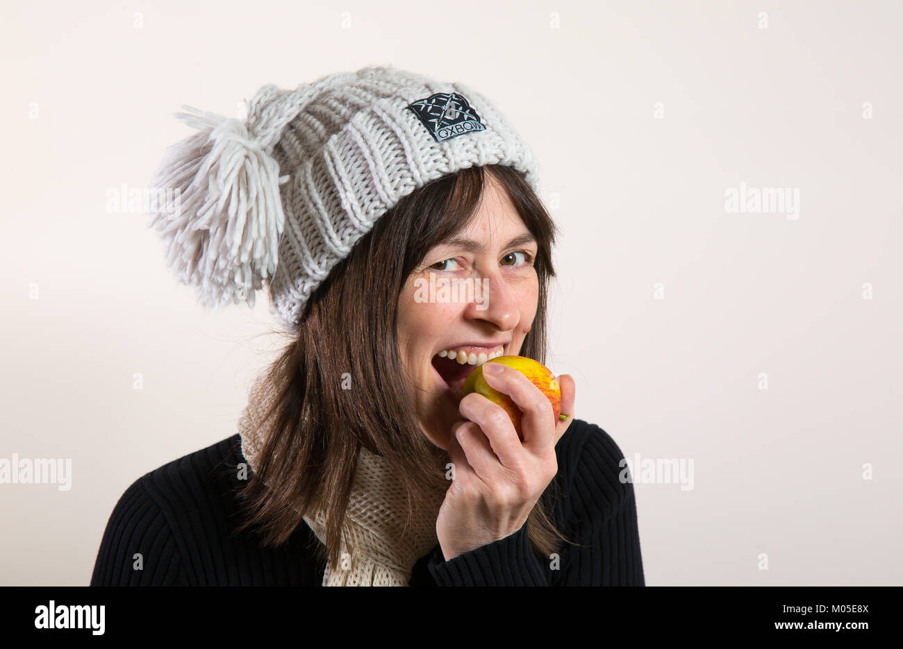 Vue rapprochée isolée de la femme en hiver chapeau de galet mangeant de la pomme à l'intérieur avec fond blanc. Banque D'Images