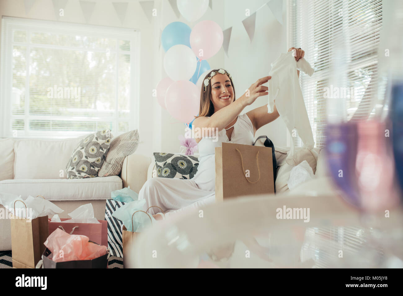 Femme enceinte cadeau après l'ouverture d'un nouveau parti de douche de bébé à la maison. Mère prévoyante regardant les vêtements de bébé à la maison. Banque D'Images