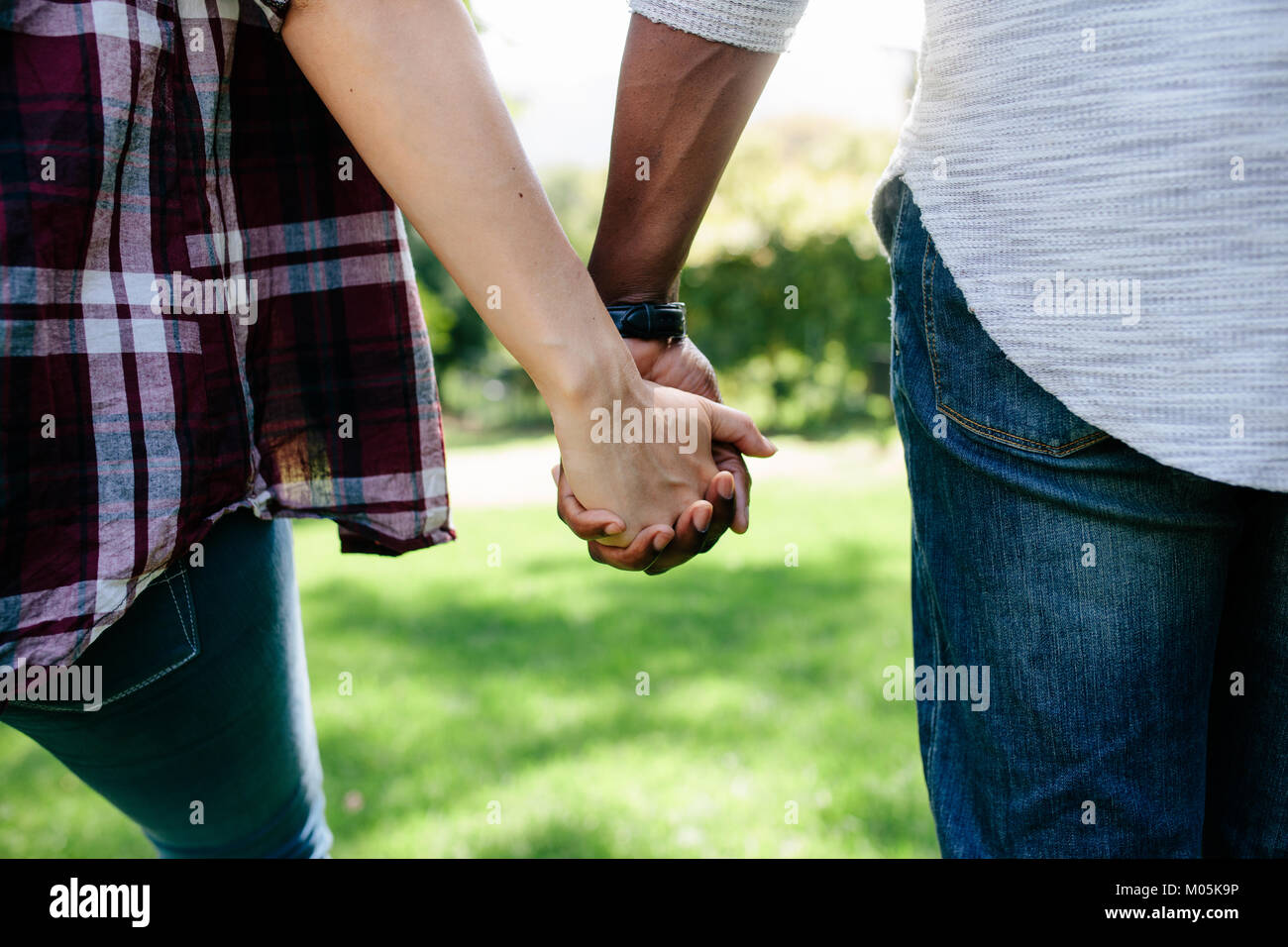 Close up of couple holding hands and walking outdoors. Vue arrière de l'homme et de la femme tenant la main de l'autre tout en marchant dans un parc. Banque D'Images