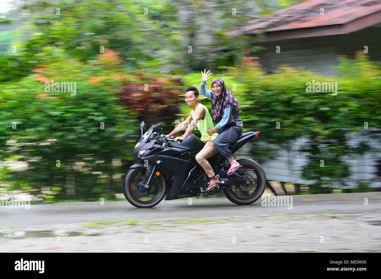 Happy smiling couple malais sur une moto en agitant, Sukau Kinabatangan, Bornéo, Sabah, Malaisie Banque D'Images