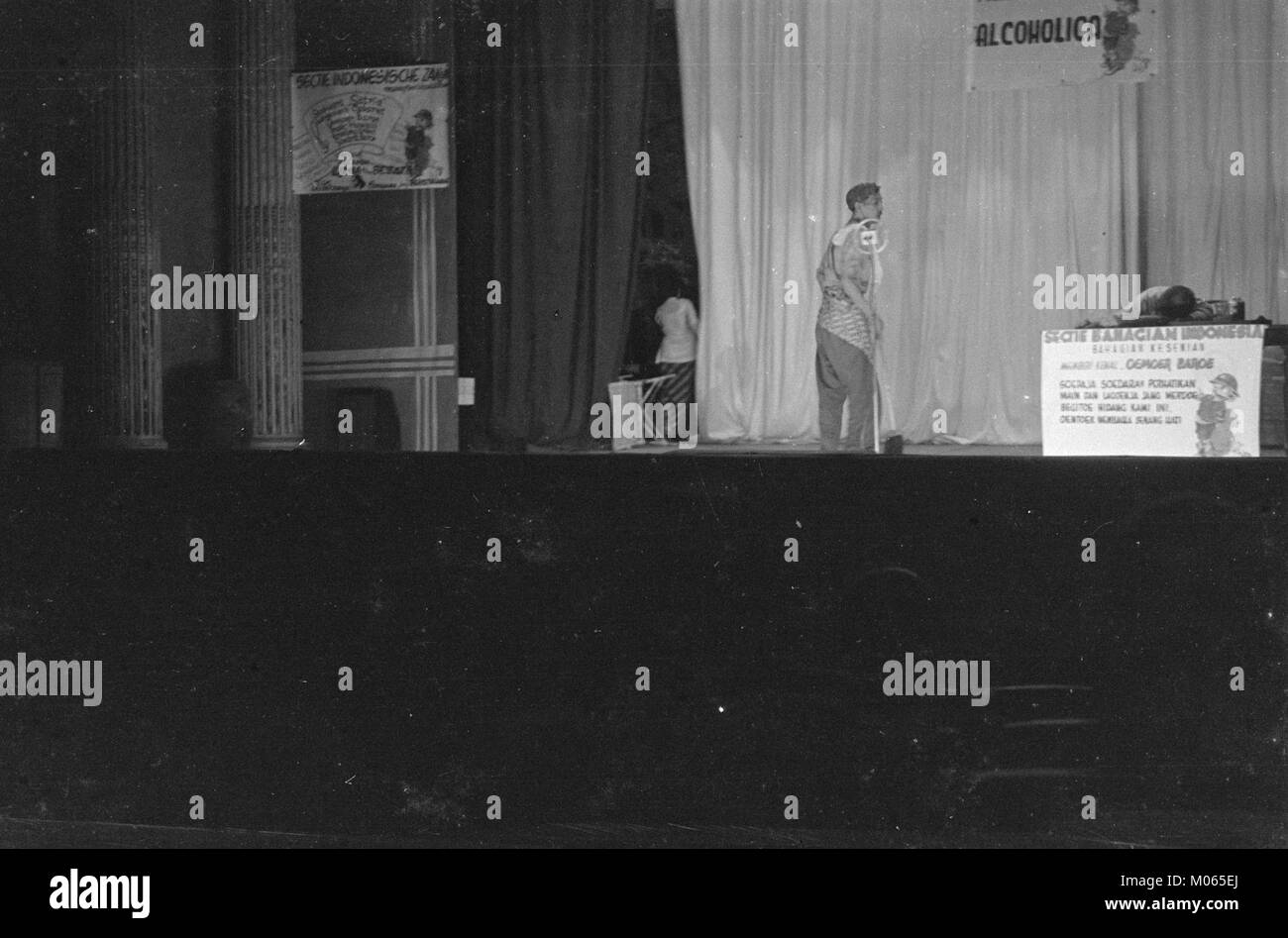 Cette image d'une performance de cabaret montre un homme assis pendu au-dessus d'une table, tandis qu'un autre se tient à côté de lui. Il capture l'atmosphère théâtrale de la performance. Banque D'Images