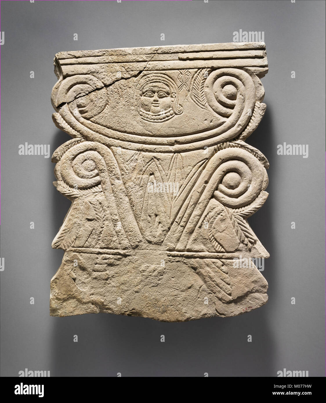 Cette stèle funéraire calcaire présente des volutes et une tête de Hathor, reflétant l'art funéraire égyptien antique et le symbolisme religieux. Banque D'Images