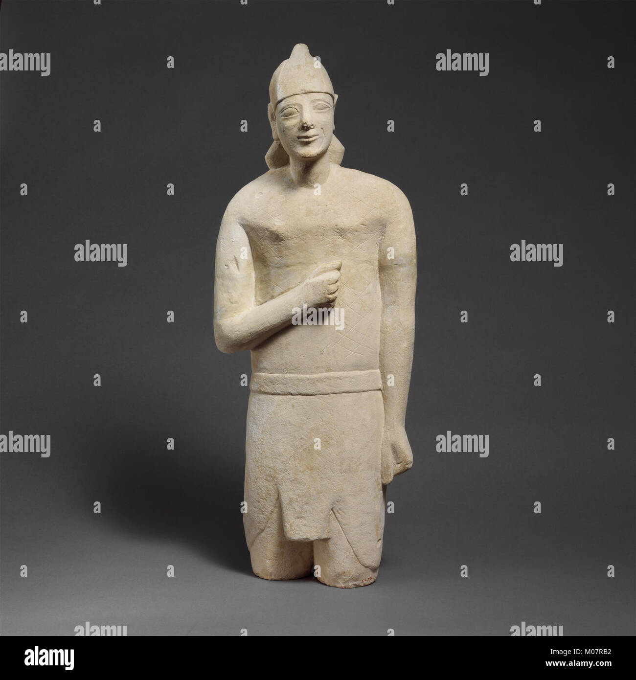 Statuette en pierre calcaire d'un homme imberbe votary dans Egyptianizing dress portant un casque rencontré DP204726 Banque D'Images