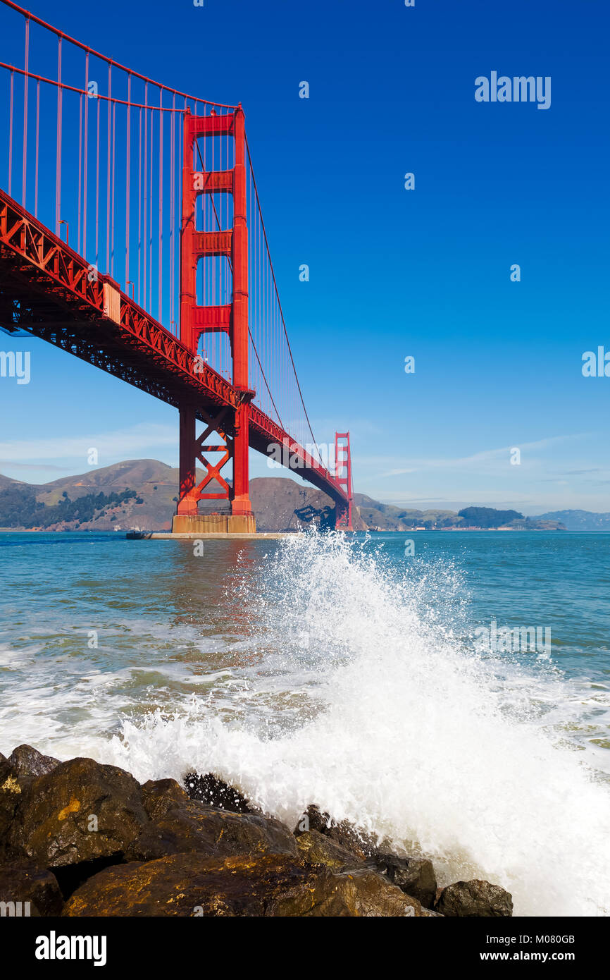 Golden Gate Bridge vu du dessous avec des projections d'une vague de l'océan dans l'avant-plan. Banque D'Images