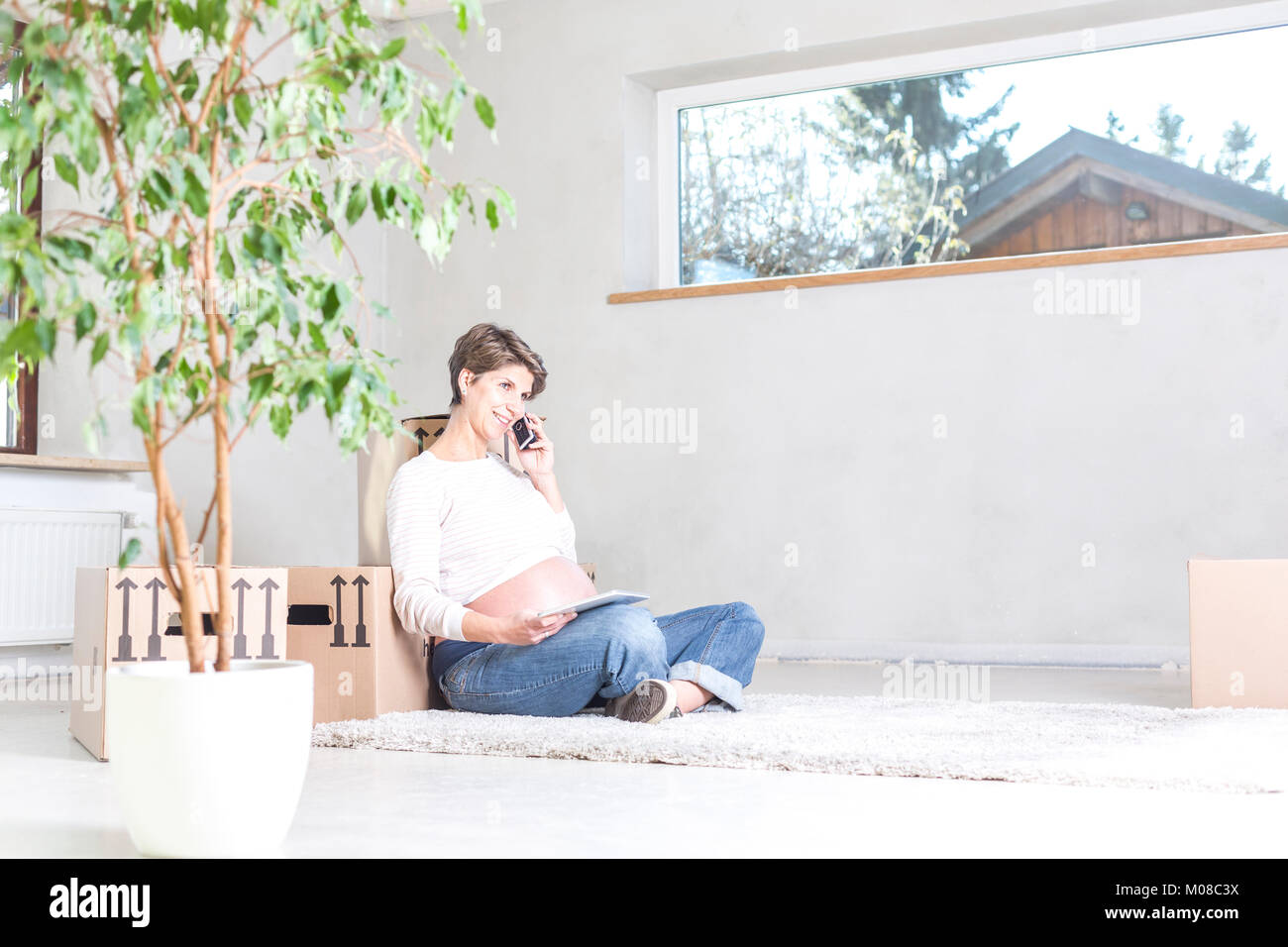 Expecting woman sitting on floor dans la nouvelle maison pendant la réinstallation Banque D'Images