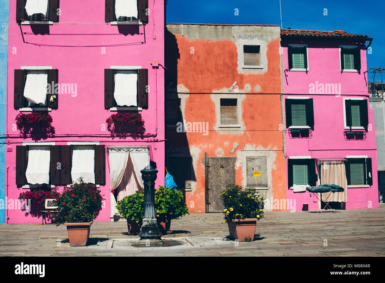 Rose et orange de maisons dans une ville vide place avec fontaine d'eau public de l'hiver dans l'île de Burano, Venise, Italie. Banque D'Images