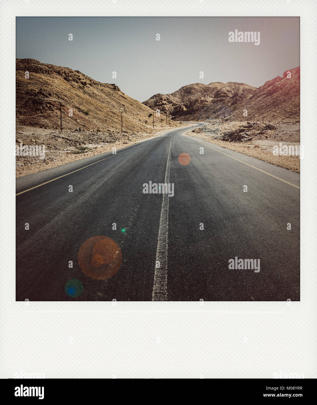 Une route goudronnée qui passe à travers les montagnes arides dans le Sultanat d'Oman dans le gouvernorat d'Al Wusta (vintage Polaroid avec cadre effet) Banque D'Images