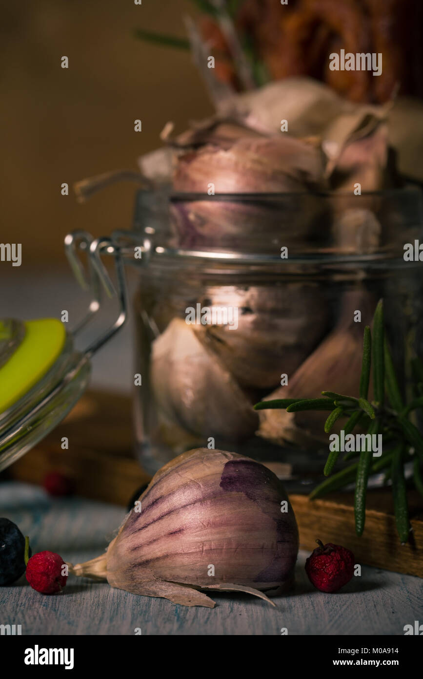 Photo verticale de plusieurs gousses d'ail. Les gousses ont une peau sombre avec teinte violette. Légume est placé dans un bocal en verre avec couvercle qui a joint vert Banque D'Images