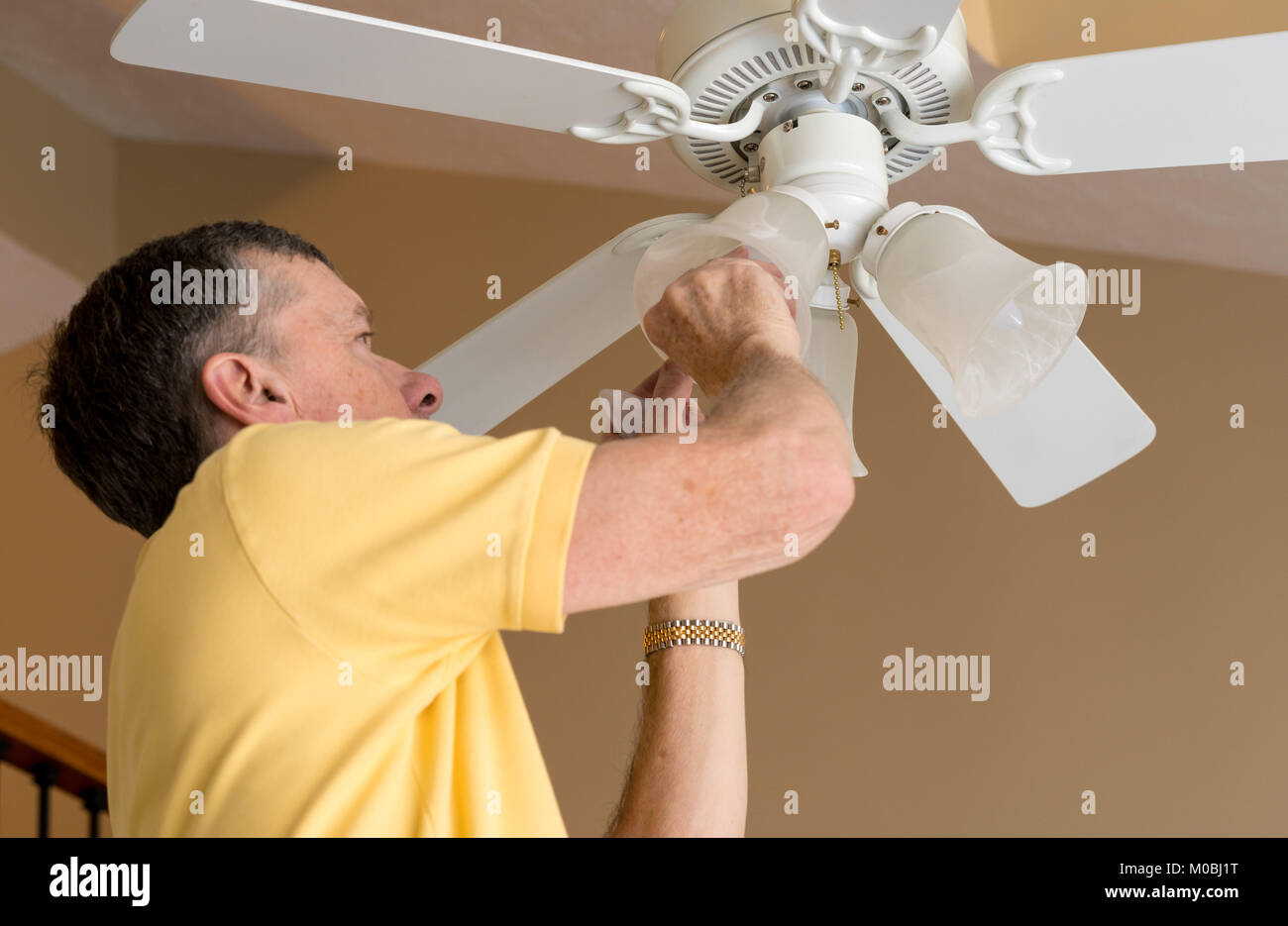 Young man de remplacer une ampoule dans un ventilateur de plafond et la lumière Banque D'Images