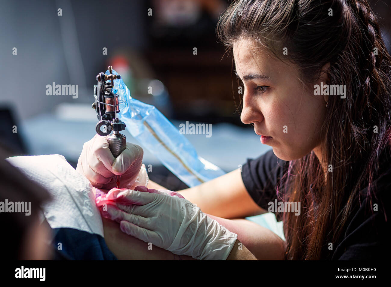 Jeune femme brune maître tatouage tatouage faisant d'un petit oiseau rouge avec machine à tatouer, close-up Banque D'Images Jeune femme brune maître tatouage tatouage faisant d'un petit oiseau rouge avec machine à tatouer, close-up Banque D'Images