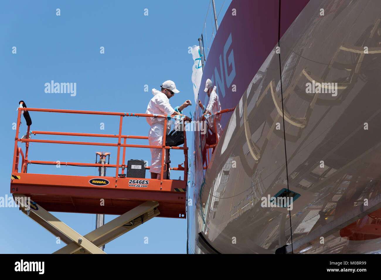 Front de mer du Cap Afrique du Sud. Décembre 2017. La Volvo Ocean Race. Bateau de course Dongfeng. L'application du ruban de masquage pour la coque par membre de l'équipe à l'aide de la SCIS Banque D'Images