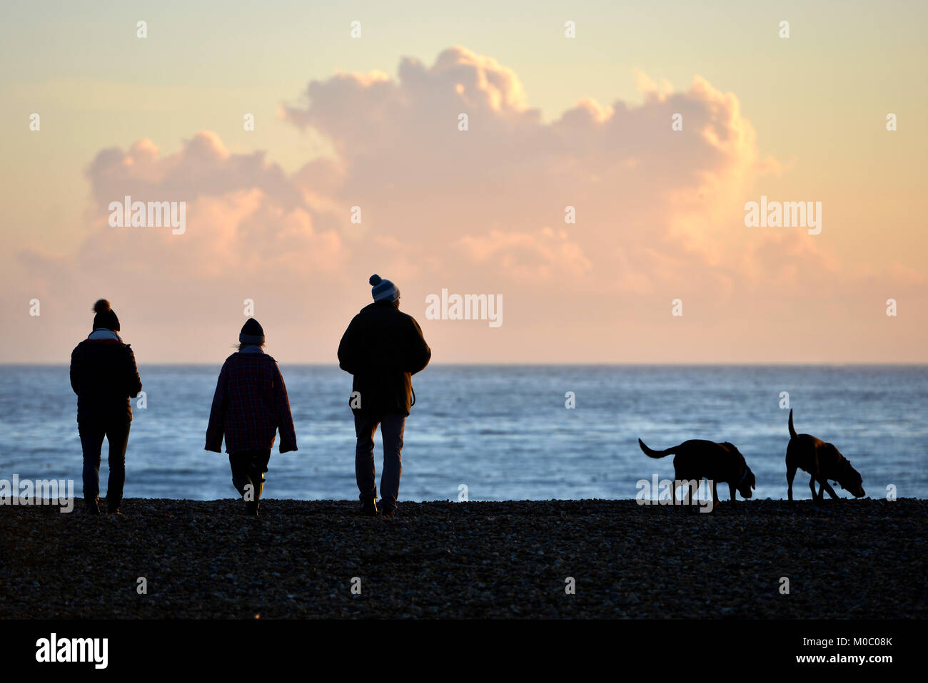 Trois personnes marchant deux chiens sur la plage au coucher du soleil, l'automne ou hiver Banque D'Images