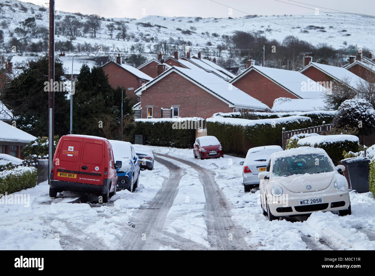 Voitures garées sur les sentiers avec centre clair de rue de banlieue recouverts de neige en Irlande du Nord Belfast Banque D'Images