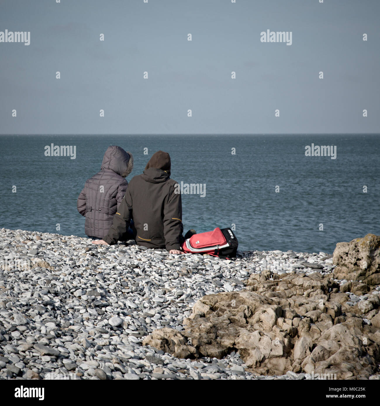 Deux adolescents de blasons et capots cailloux assis face à la mer sur une journée froide Banque D'Images