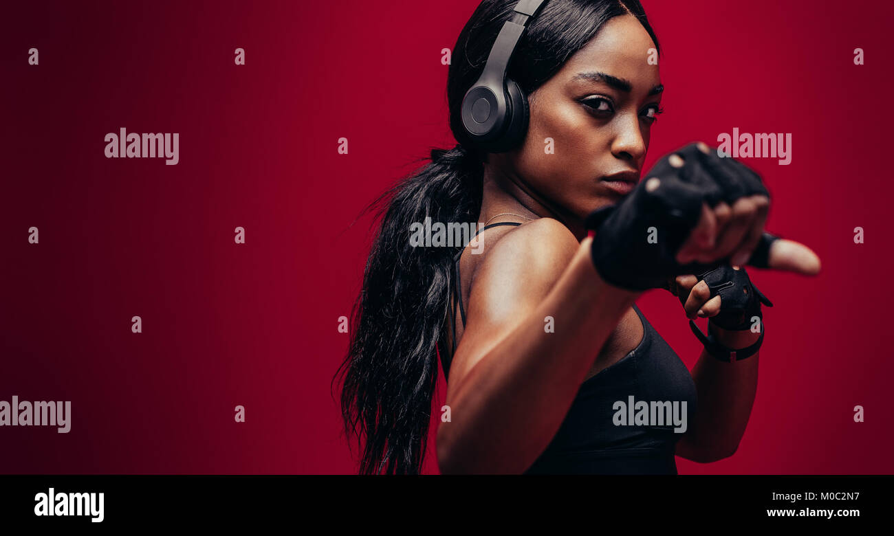 Jeune femme forte avec un casque pratique de la boxe. African boxer exerçant sur fond rouge Banque D'Images Jeune femme forte avec un casque pratique de la boxe. African boxer exerçant sur fond rouge Banque D'Images