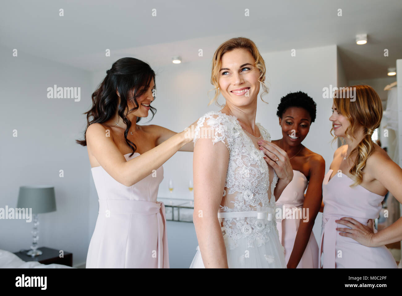 Mariée et demoiselles lors des préparatifs du mariage. Les amis s'habiller la mariée de mariage dans une chambre d'hôtel. Banque D'Images