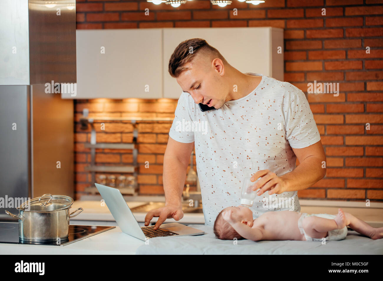 L'alimentation de bébé son père tout en essayant de travailler sur ordinateur portable Banque D'Images