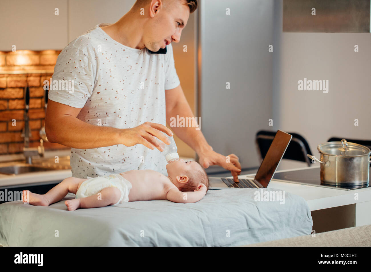 Papa essaie de travailler sur les ordinateurs portables et de parler au téléphone avec son nouveau-né dans la maison Banque D'Images