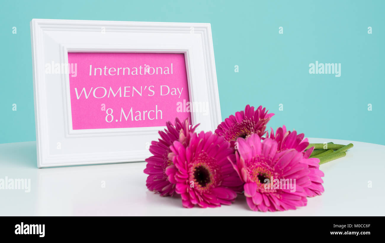 Bonne Journée de la femme de couleur pastel bleu bonbon rose foncé sur fond d'ions et la table gerberas cadre photo Blanc avec Happy Womens Day message. Banque D'Images