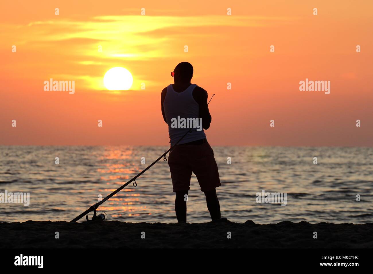 Pêcheur en mer contre le coucher du soleil Banque D'Images