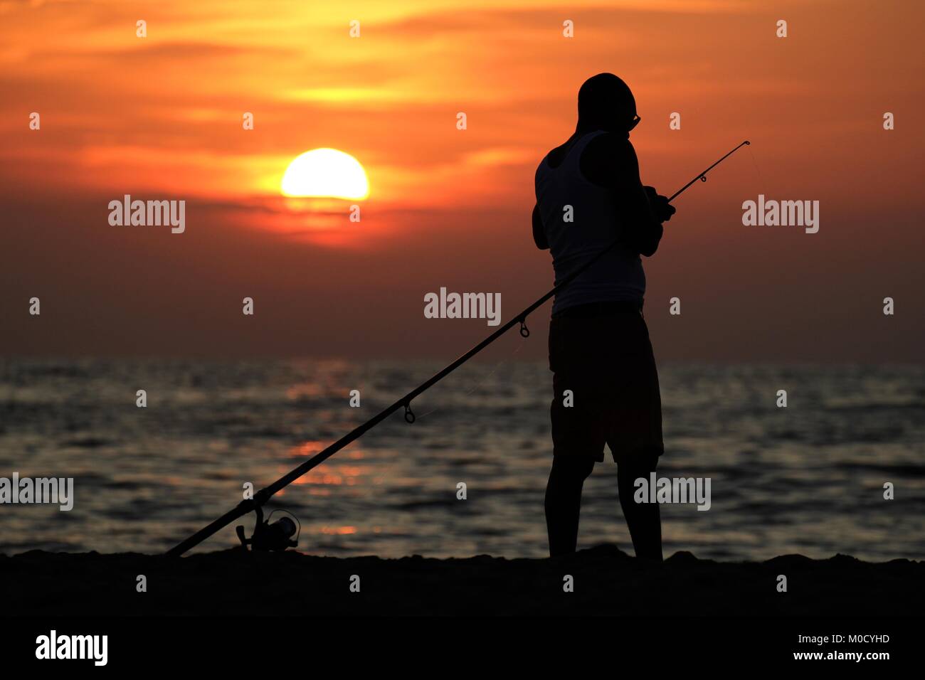 Pêcheur en mer contre le coucher du soleil Banque D'Images