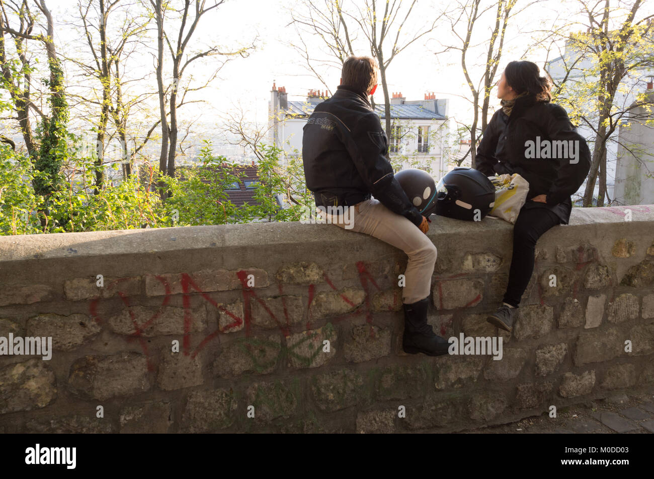 Deux motards chat assis sur un mur en pierre avec une vue sur Paris à Montmartre, France avec motorbike helmets entre eux Banque D'Images