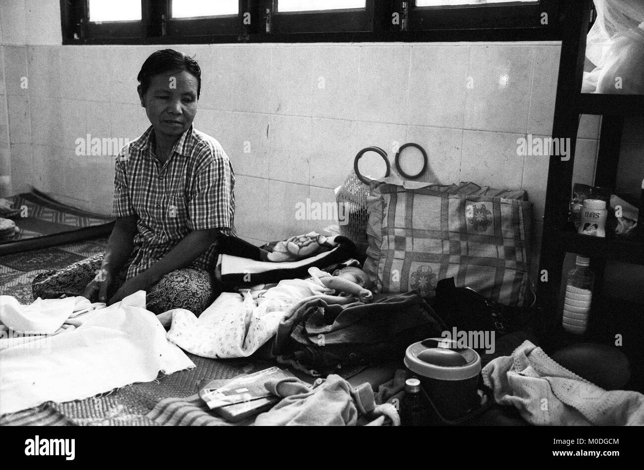 Une mère veille sur son enfant malade dans le service de pédiatrie à la clinique Mae Tao sur la frontière thaïlando-birmane. Environ 300 personnes par jour reçoivent des soins gratuits à la clinique, la plupart étant des travailleurs migrants et réfugiés qui ont franchi la frontière de la Birmanie (Myanmar) pour échapper à la pauvreté désespérée et la persécution du régime militaire. Les soins de santé sont tous mais inexistante en Birmanie, où moins de 2  % du PIB est consacré à la santé et l'éducation combinées. Banque D'Images