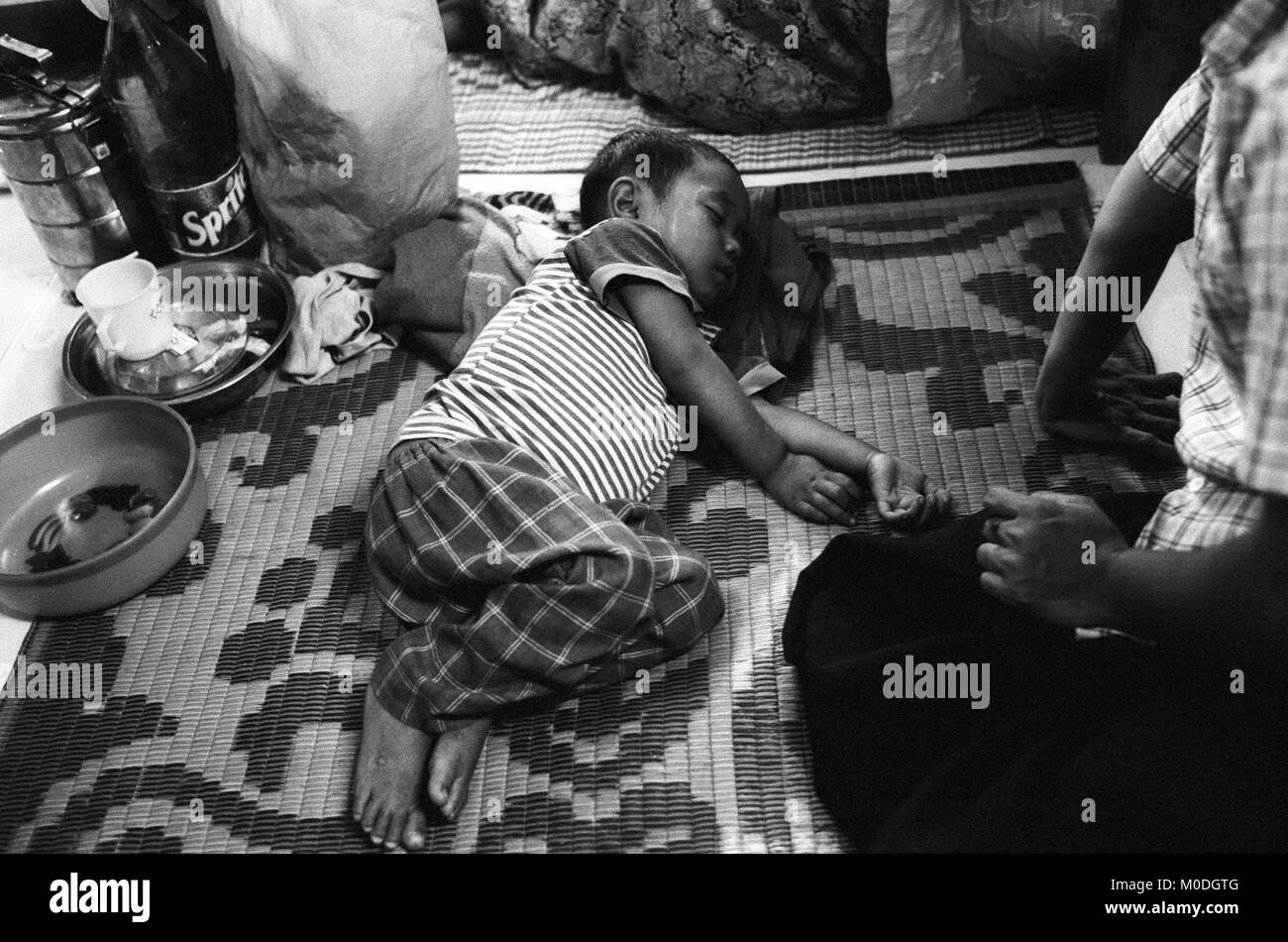 Avec un jeune enfant souffrant de dysenterie aiguë se trouve dormant dans le service de pédiatrie à la clinique Mae Tao sur la frontière thaïlando-birmane. Environ 300 personnes par jour reçoivent des soins gratuits à la clinique, la plupart étant des travailleurs migrants et réfugiés qui ont franchi la frontière de la Birmanie (Myanmar) pour échapper à la pauvreté désespérée et la persécution du régime militaire. Les soins de santé sont tous mais inexistante en Birmanie, où moins de 2  % du PIB est consacré à la santé et l'éducation combinées. Banque D'Images