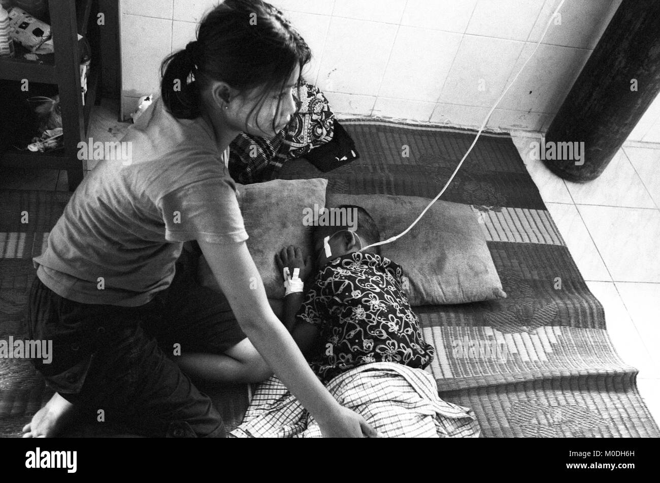 Une mère veille sur son jeune fils dans le service de pédiatrie à la clinique Mae Tao sur la frontière thaïlando-birmane. Environ 300 personnes par jour reçoivent des soins gratuits à la clinique, la plupart étant des travailleurs migrants et réfugiés qui ont franchi la frontière de la Birmanie (Myanmar) pour échapper à la pauvreté désespérée et la persécution du régime militaire. Les soins de santé sont tous mais inexistante en Birmanie, où moins de 2  % du PIB est consacré à la santé et l'éducation combinées. Banque D'Images