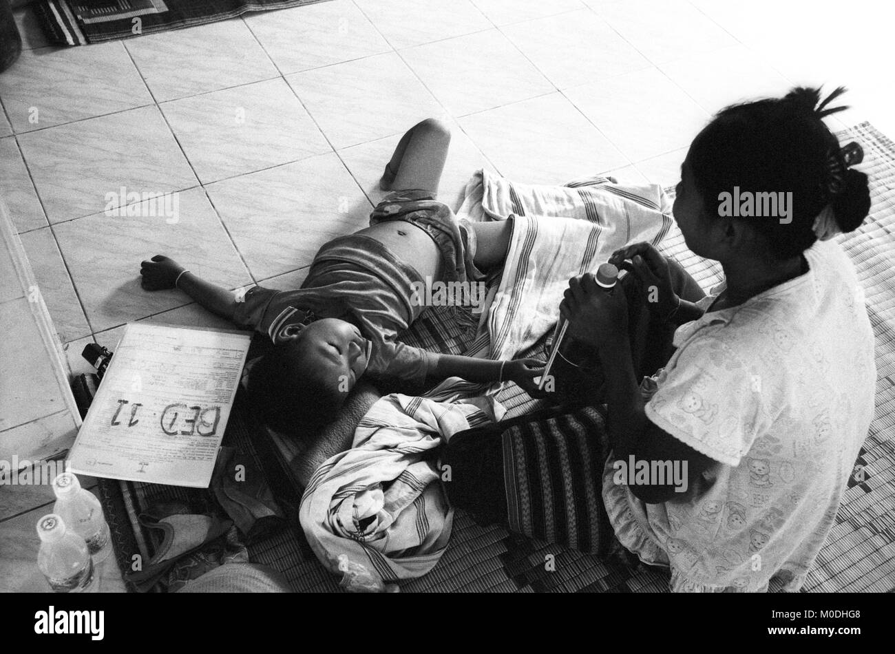 Une mère veille sur son jeune garçon atteint de paludisme dans le service de pédiatrie à la clinique Mae Tao sur la frontière thaïlando-birmane. Environ 300 personnes par jour reçoivent des soins gratuits à la clinique, la plupart étant des travailleurs migrants et réfugiés qui ont franchi la frontière de la Birmanie (Myanmar) pour échapper à la pauvreté désespérée et la persécution du régime militaire. Les soins de santé sont tous mais inexistante en Birmanie, où moins de 2  % du PIB est consacré à la santé et l'éducation combinées. Banque D'Images