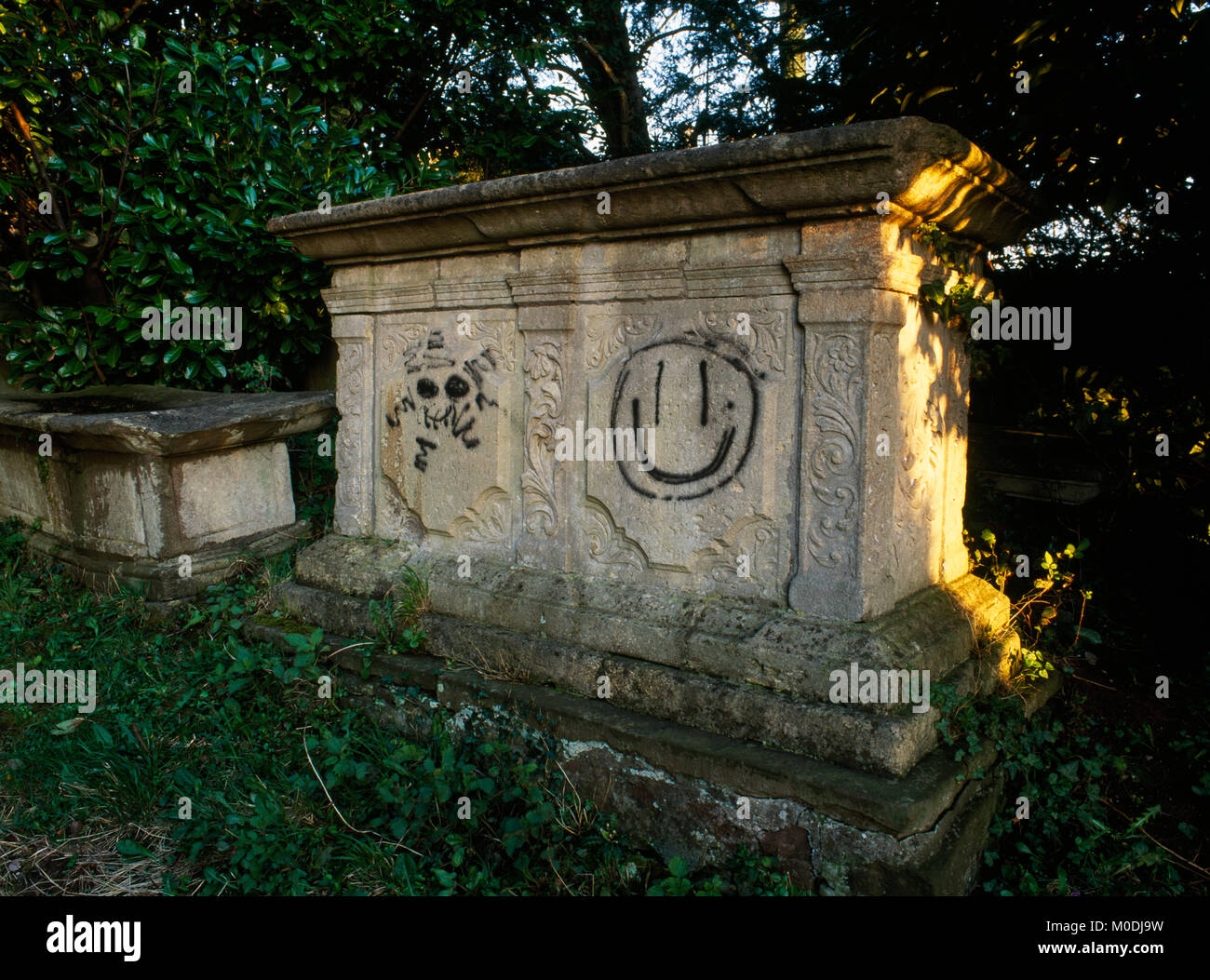 Graffiti moderne de deux visages peint à la bombe sur la poitrine de style géorgien orné tombeau à St Mary the Virgin's Church cimetière, Berkeley, Gloucestershire. Banque D'Images