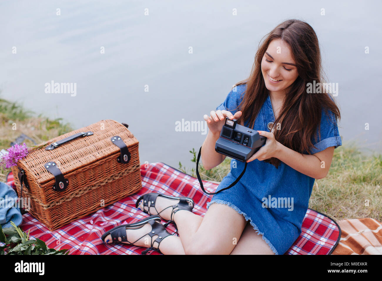 Femme assise sur une couverture de pique-nique tenant un appareil photo instantané vintage Banque D'Images