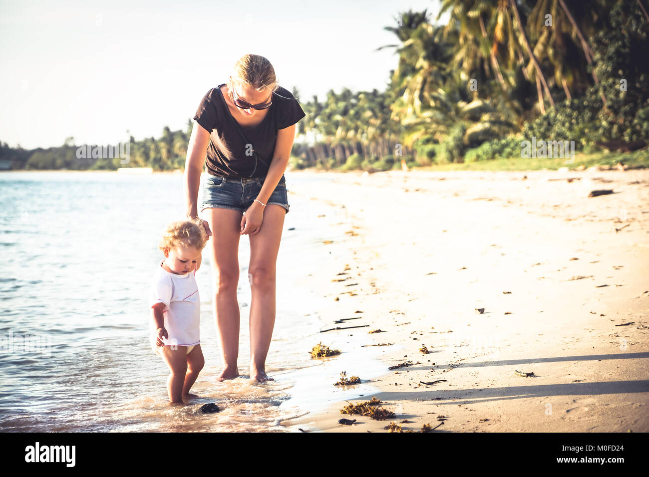 Mère et fille bébé marche sur plage avec holding hands Banque D'Images